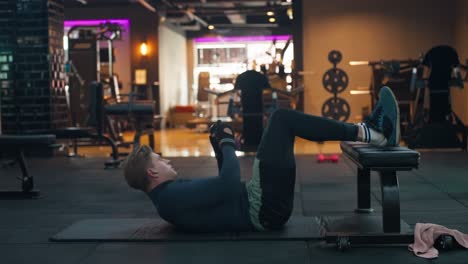 man doing twisted crunches with kettlebell exercise for the abs and obliques in modern gym - static slow motion