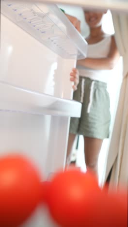 person opening refrigerator to get tomatoes