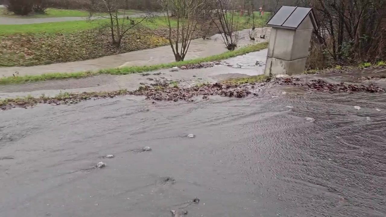 Silný déšť způsobující přetečení bahnitého potoka a zaplavení asfaltové silnice ve venkovské oblasti.