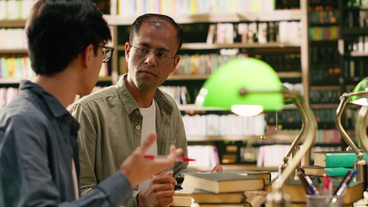 Mentor and student discussing research over open books at wooden library table