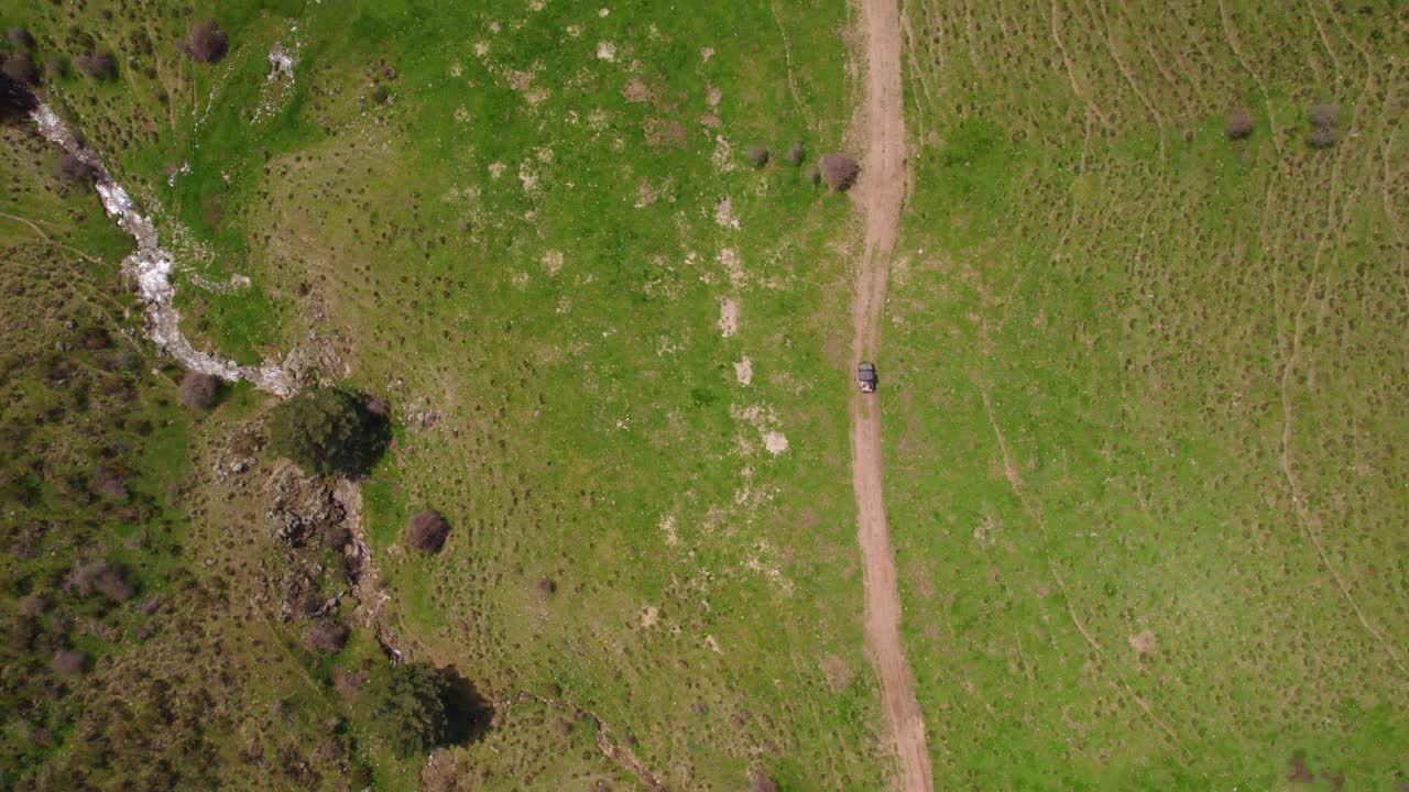 toma aérea de arriba hacia abajo de la conducción de automóviles 4x4 en un camino rural entre campos verdes durante la luz del sol