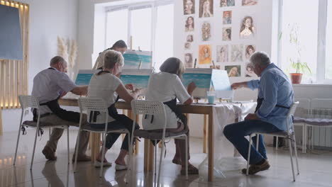 slow motion old people attend drawing courses. the teacher helps pensioners who attend drawing courses to draw. a group of retired friends at a drawing lesson