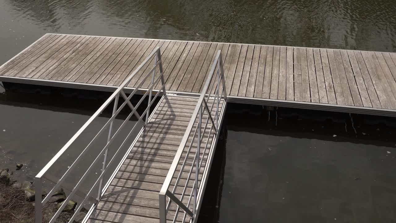 A walkway made of wood and metal to access a dock for boats. All of it is set on a river at the beginning of spring.