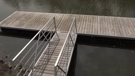 a walkway made of wood and metal to access a dock for boats. all of it is set on a river at the beginning of spring.