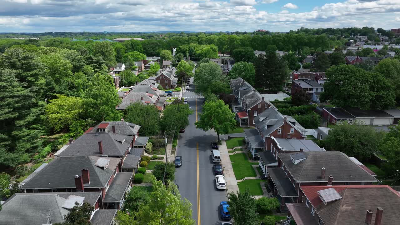 Typical two story homes with porch in American neighborhood. Green trees blossoming in summer. Descend drone wide shot. Cars along street at sidewalk.