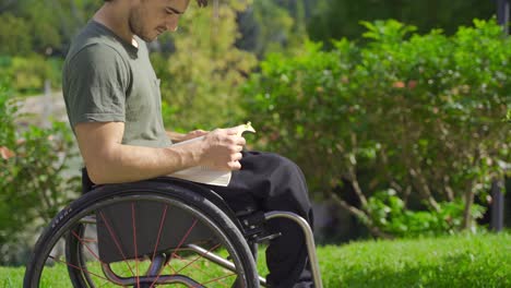 young man with physical disability is reading a book outdoors.