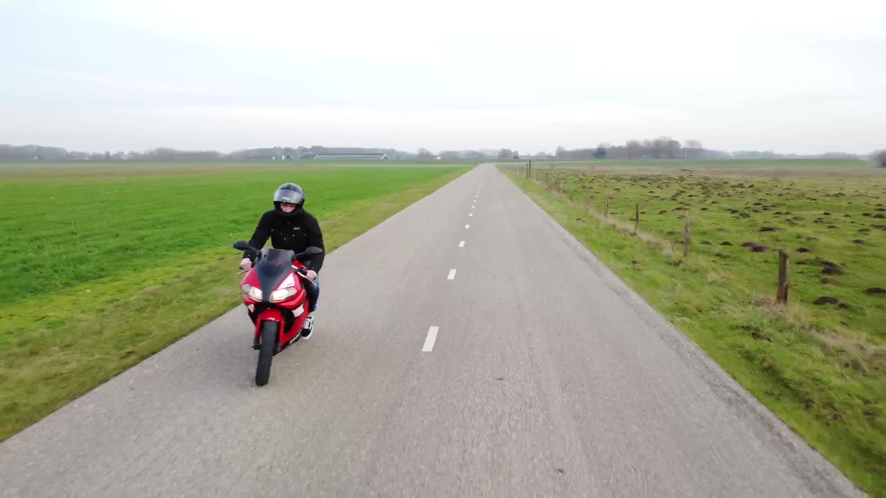 그의 앞에 무인 항공기와 함께 길을 운전하는 오토바이의 샷