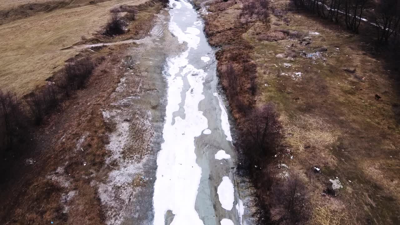 Съемка с дрона: лес и замерзшая загородная река поздней осенью.