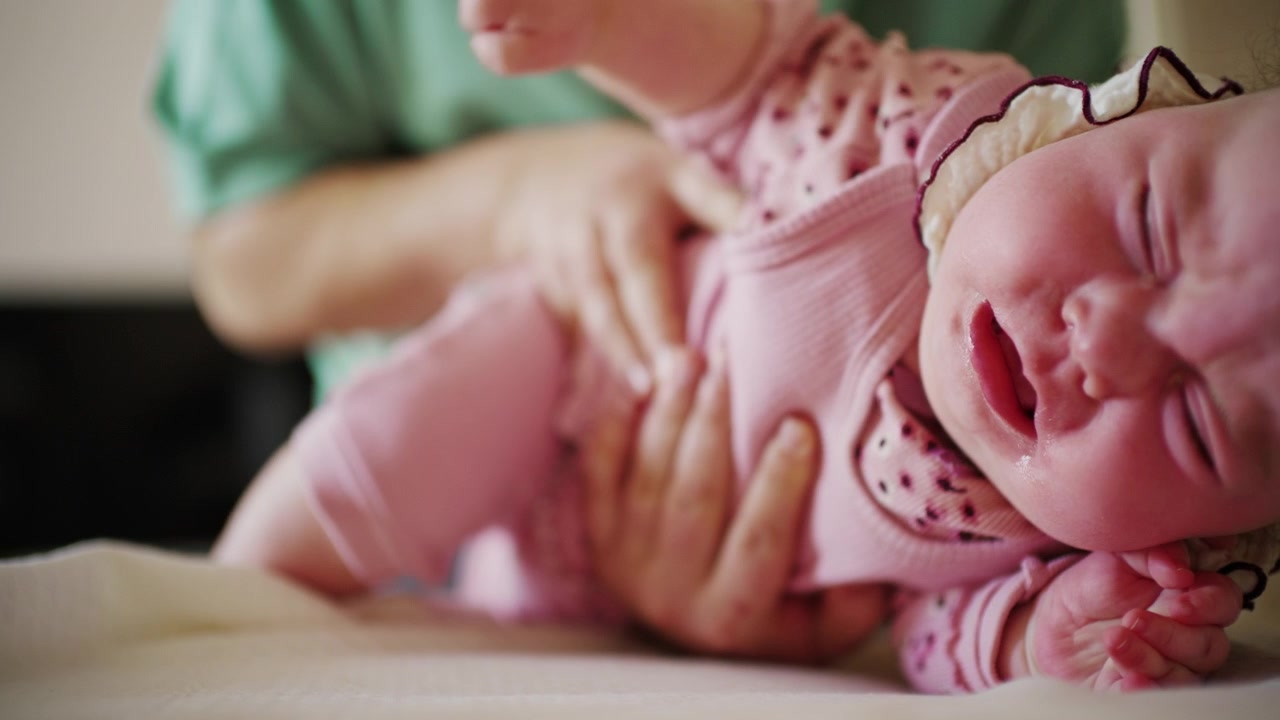 Primo piano di un bambino che mostra una leggera smorfia o disagio mentre è tenuto in braccio da un adulto
