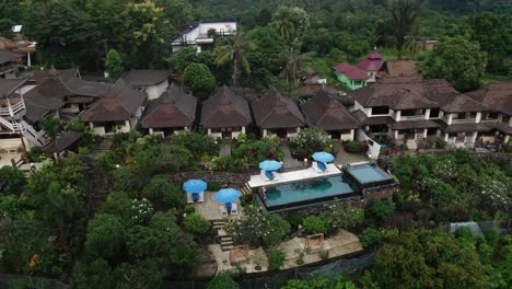 orbital aerial shot over a luxury villa complex in asia, a man standing at the swimming pool surrounded by a tropical forest