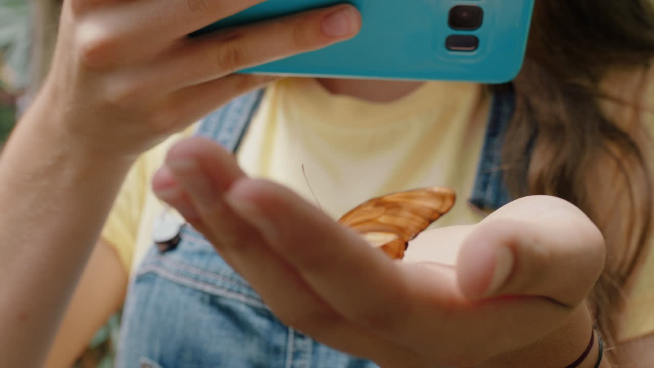 joven tomando una foto de una mariposa en la mano usando un teléfono inteligente disfrutando de una excursión al zoológico compartiendo la conciencia ambiental en las redes sociales 4k