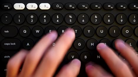 close-up of hands typing on a round-key black keyboard