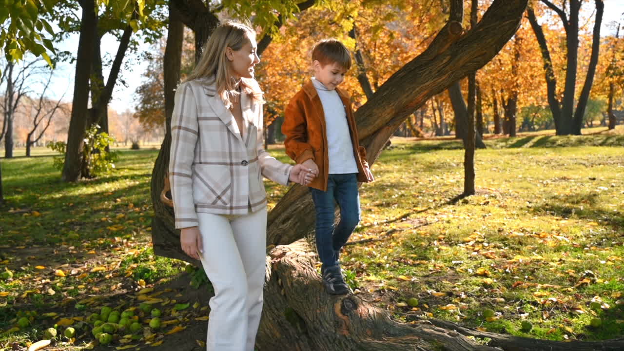 Happy family in an autumn park. Mother walking with her son and talking, yellowed trees around. Slow motion
