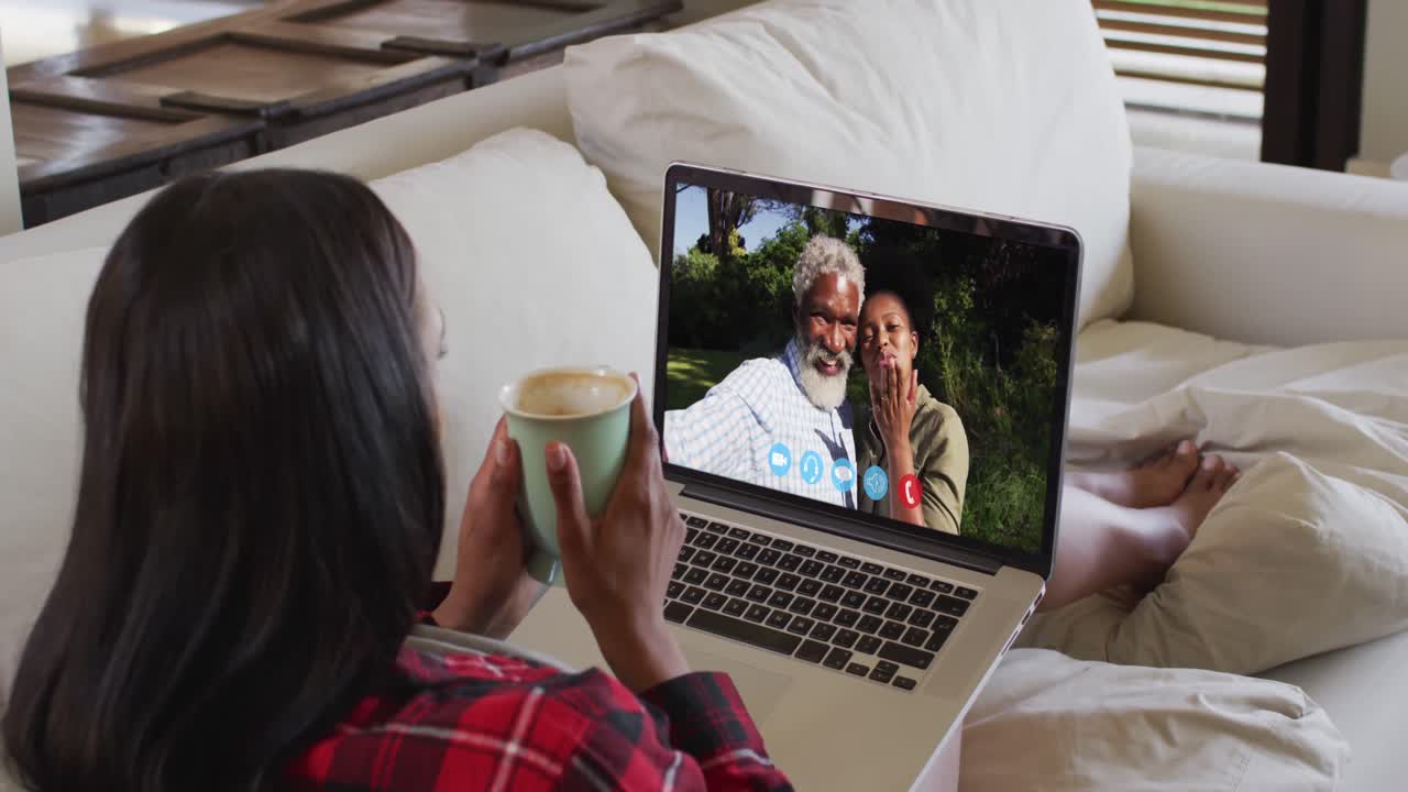African american woman holding a coffee cup having a video call on laptop sitting on couch at home