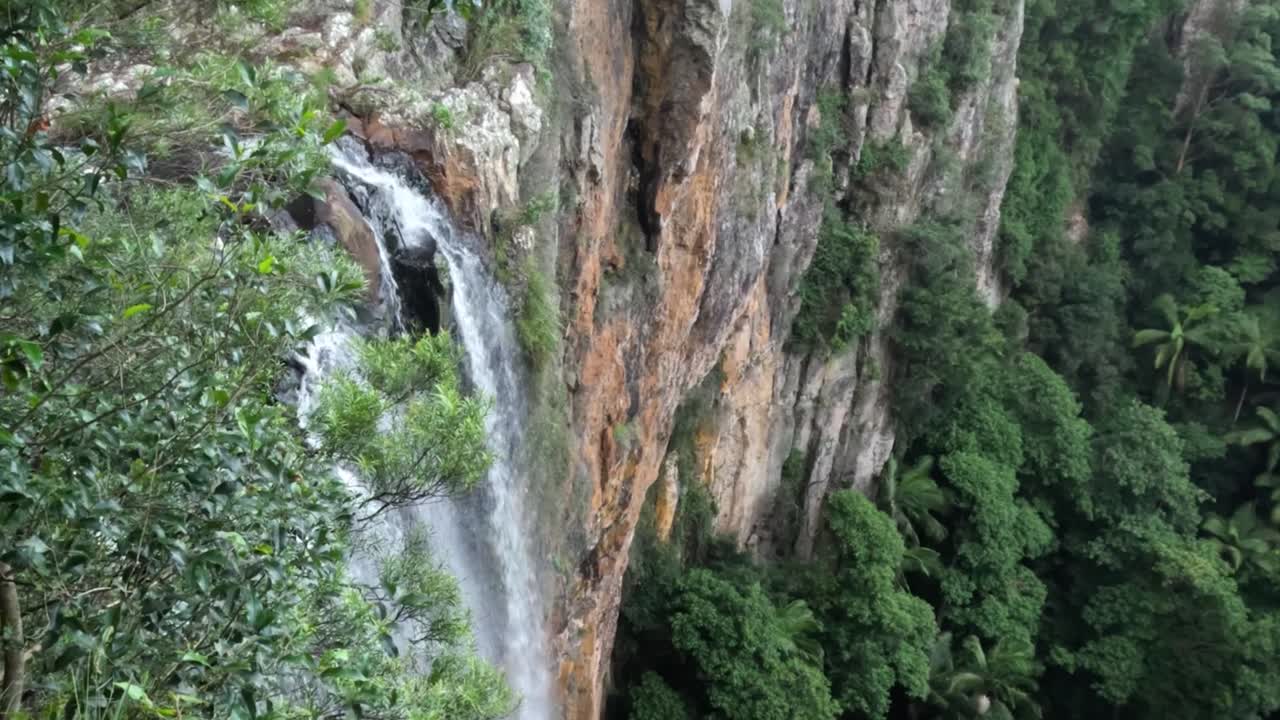 A waterfall flows down a rugged cliff surrounded by dense green foliage.