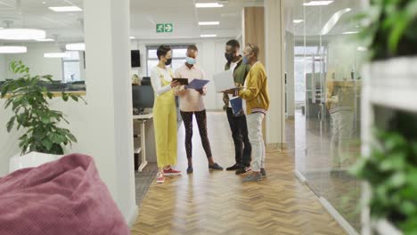 grupo diverso de colegas de negocios masculinos y femeninos que usan máscaras faciales, trabajando en la oficina