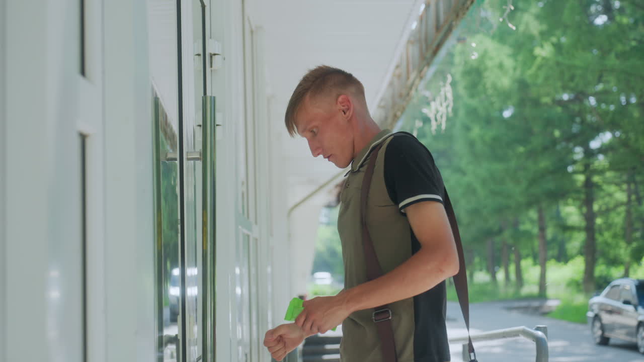 Nuori mies puhdistaa ovenkahvaa huolellisesti, miespuolinen henkilö desinfioi varovasti oven lukon rievulla, nuori valkoihoinen mies puhdistaa huolellisesti ovenkahvan varovaisesti käyttäen paperipyyhettä.