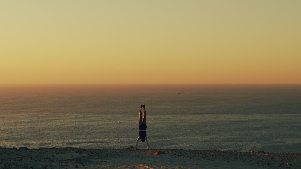Persona che fa la verticale sul bordo di una scogliera con vista sull'oceano al tramonto