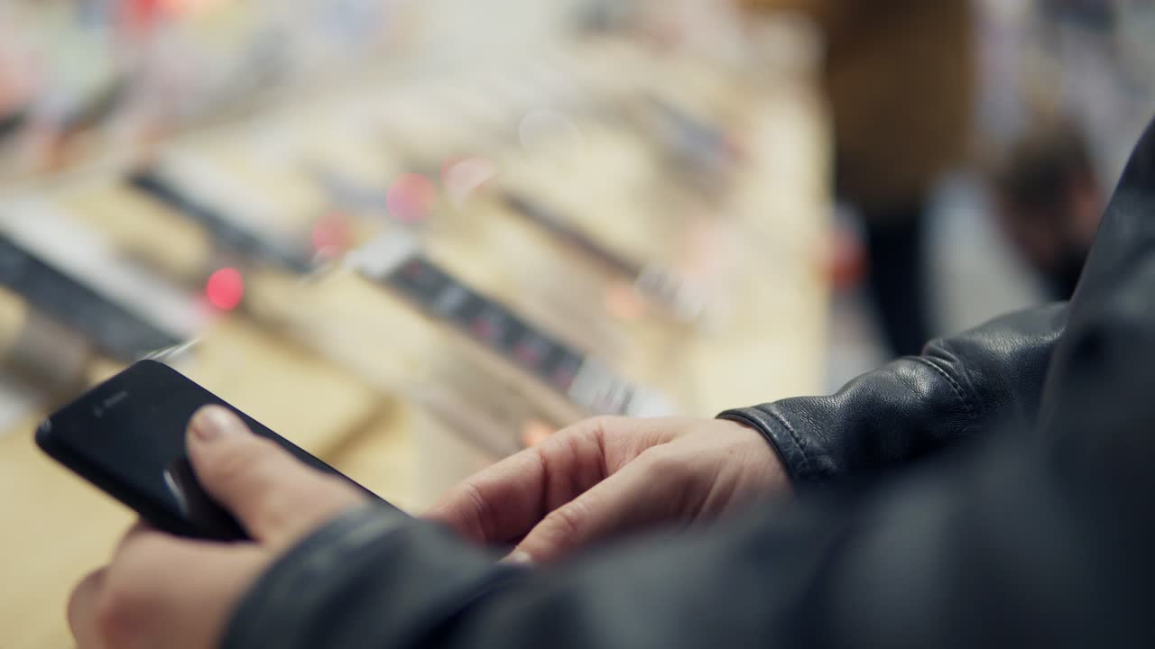 Closeup view of a young man's hands choosing a new mobile phone in a shop. He is trying how it works