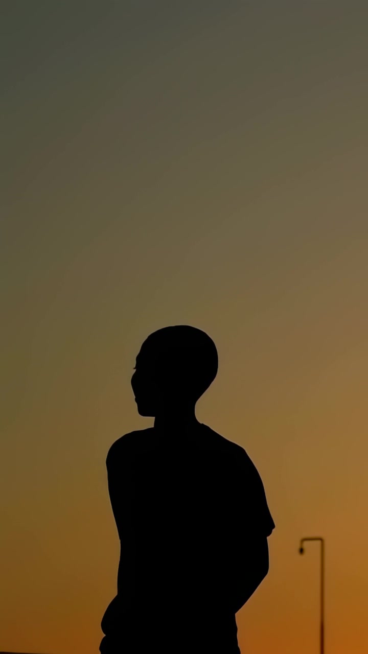 垂直影片：日落景色中，畫面中央的青少年和一群人穿著T恤和連帽衫，在欄杆和路燈旁交談。