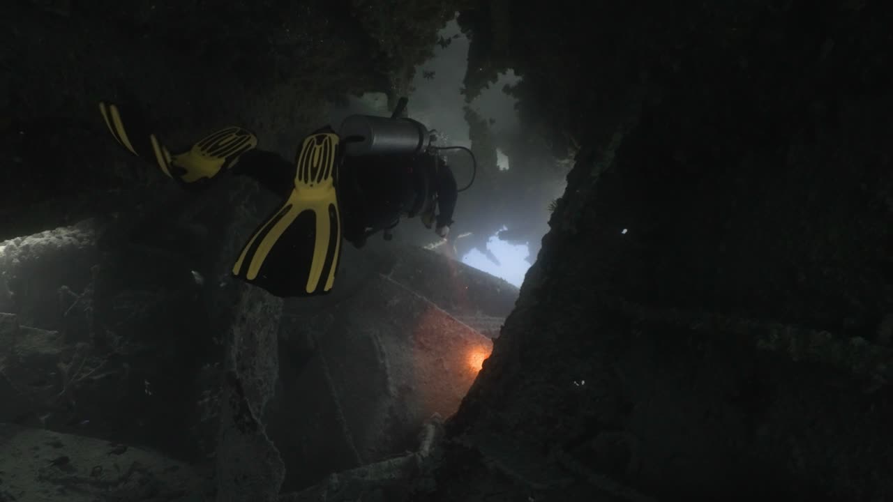 Scuba diver swimming in a very narrow pathway inside a sunken boat in 4k