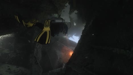 scuba diver swimming in a very narrow pathway inside a sunken boat in 4k