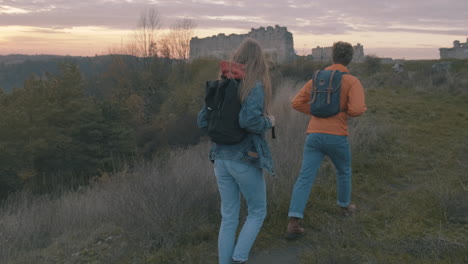 young couple of female and male hikers at the top of the mountain find ruins of an ancient castle beautiful sunset