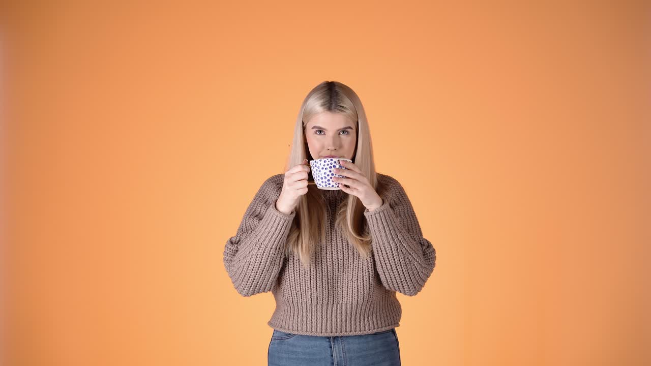 핑크색 배경에 카메라를 바라보며 커피 컵에서 마시는 예쁜 금발 여성의 초상화, 스튜디오 촬영