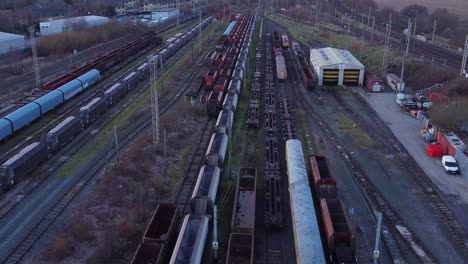 sunrise aerial view of long railroad tracks with heavy diesel locomotive carriages and cargo container yard tilt up reverse shot