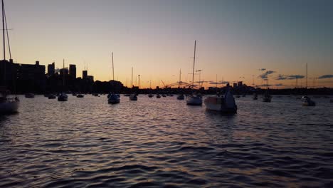 Puesta-De-Sol-En-La-Bahía-Con-La-Silueta-De-Los-Mástiles-De-Los-Veleros-Y-El-Puente-Del-Puerto-En-La-Distancia