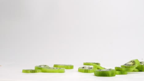 Sliced-kiwi-pieces-dropped-onto-white-studio-backdrop-in-4k-slow-motion