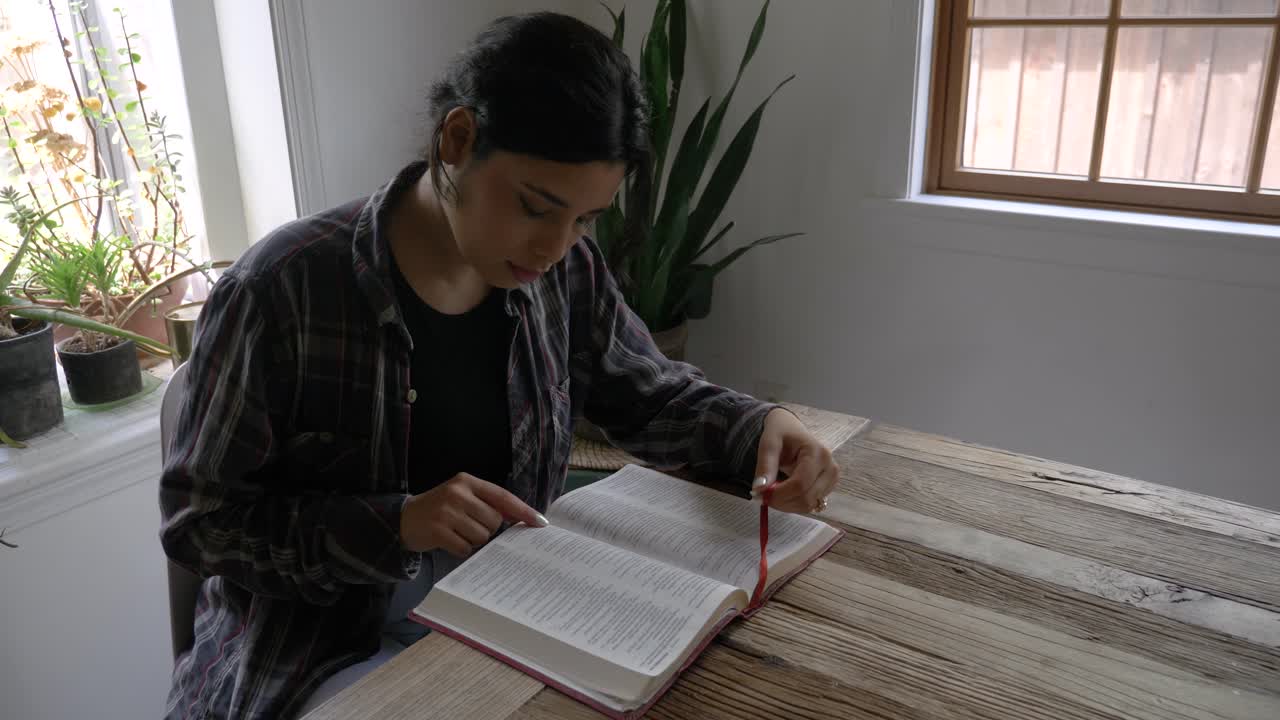 Puerto Rican female teenager reading and studying holy bible at rustic wooden table