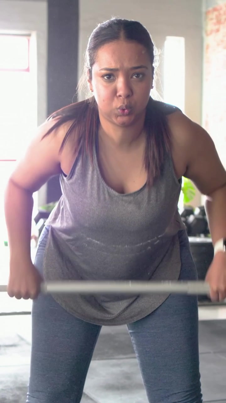 Video verticale: Donna in palestra che batte il gesso, con canotta, aggiusta la postura, afferra il bilanciere preparandosi a sollevare