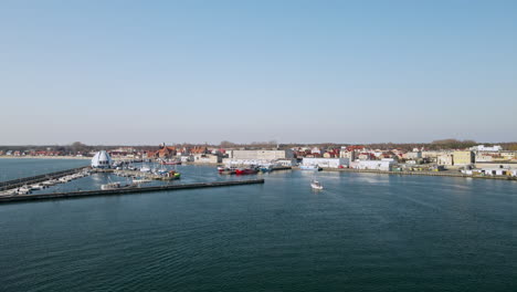 Hel-Peninsula-before-the-season,-a-white-sailboat-enters-the-harbor-on-the-calm-water-of-the-Puck-Bay,-slow-motion-aerial,-Poland