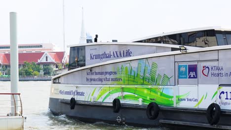 an electric ferry travels along the chao phraya river in bangkok, showcasing urban scenery and eco-friendly transport under bright daylight