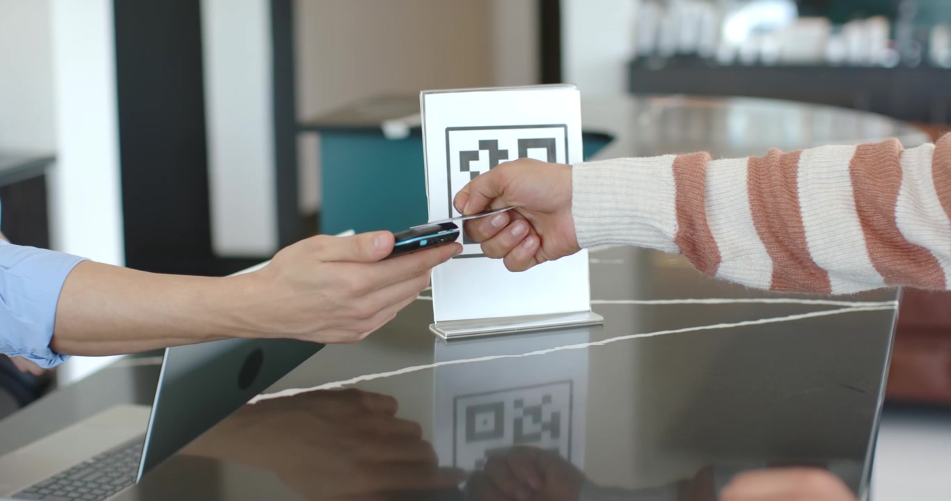 Uomo afroamericano con un laptop che tocca il telefono e presenta il terminale mentre il cliente tocca la carta per pagare.