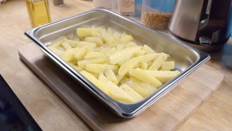 slow motion slider shot of seasoning homemade oven fries in a metal baking tray prior to cooking in the kitchen