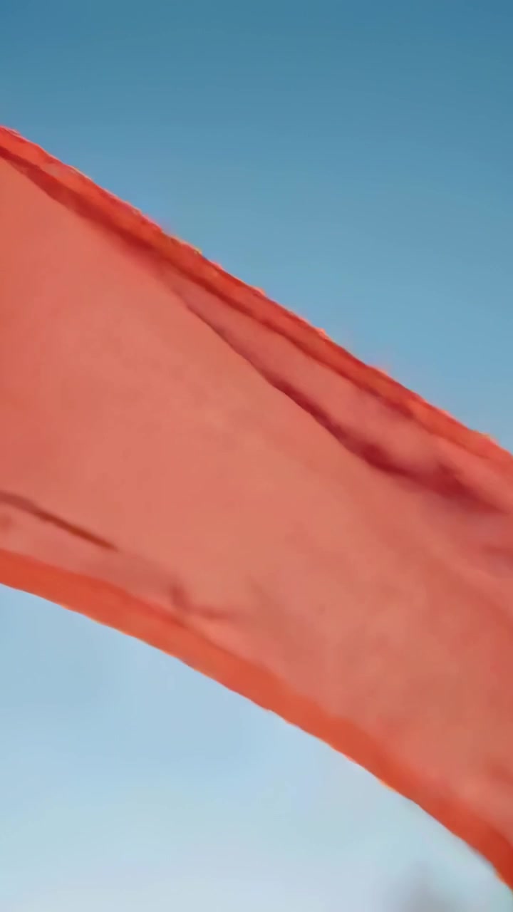 Video vertical: Tela roja ondeante y deshilachada, agitándose por el viento racheado bajo cielo abierto.