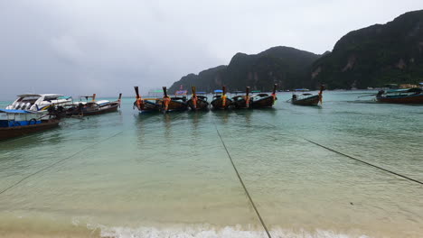 Botes-Tradicionales-De-Cola-Larga-En-La-Orilla-Del-Mar-De-Andamán-En-La-Isla-Phi-Phi-En-Tiempo-Lluvioso,-Tailandia,-Tiro-De-Retirada