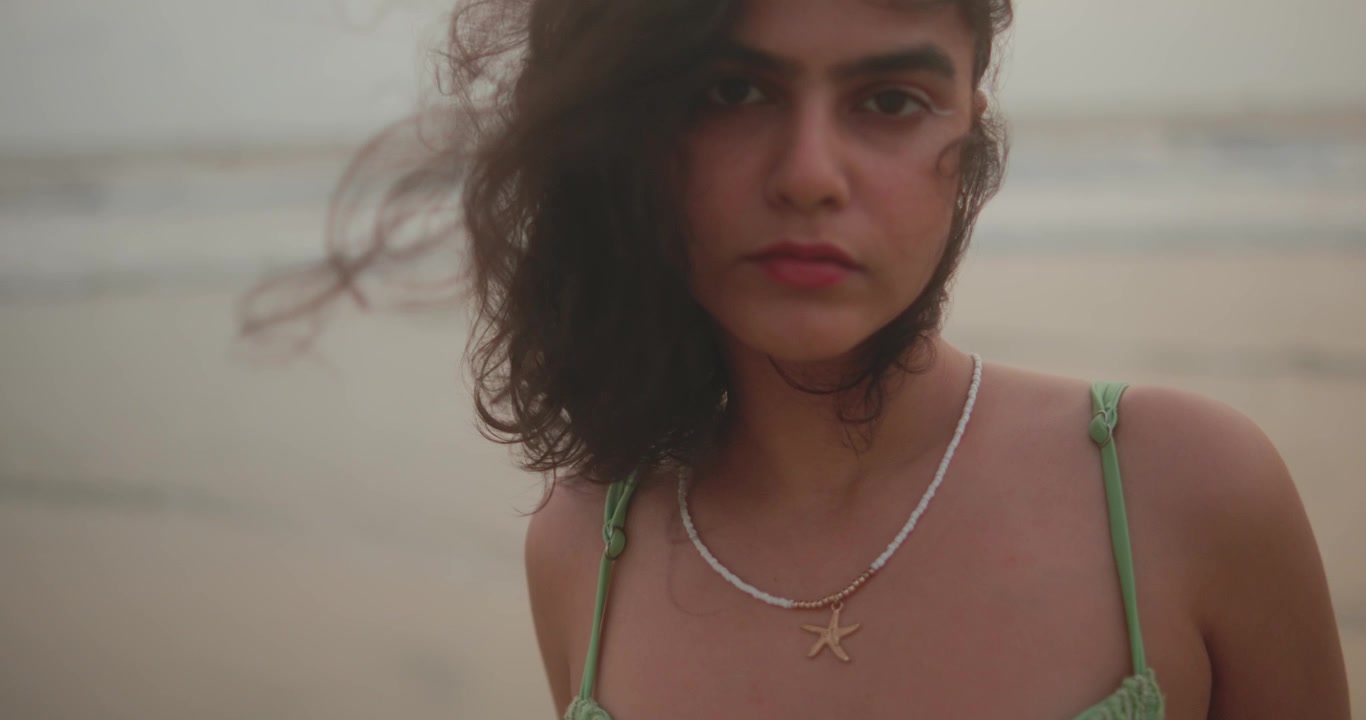 Primo piano che si avvicina a una donna sulla spiaggia con i capelli mossi dal vento.