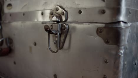 a man's hand opens the latch on a sturdy silver trunk