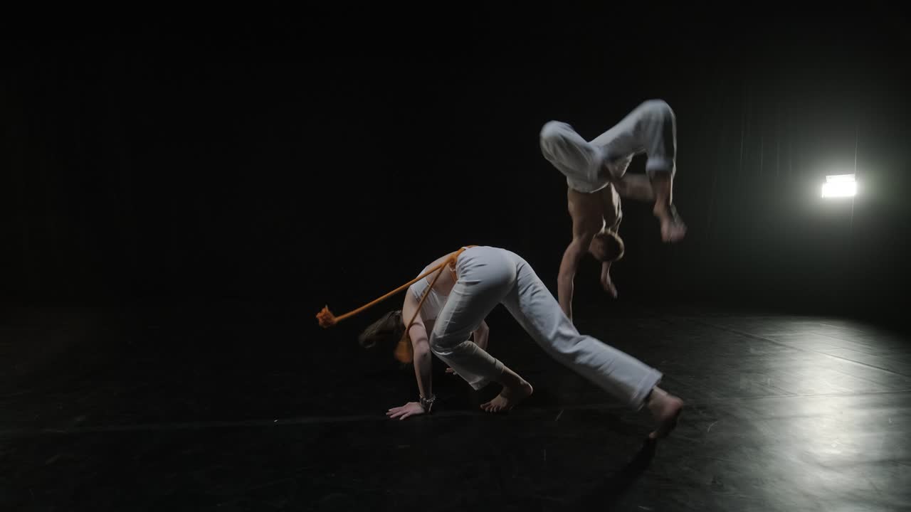 un grupo de bailarines profesionales están practicando capoeira en la oscuridad contra un foco de luz en un fondo negro de estudio. arte marcial afro-brasileño que combina elementos de la danza.