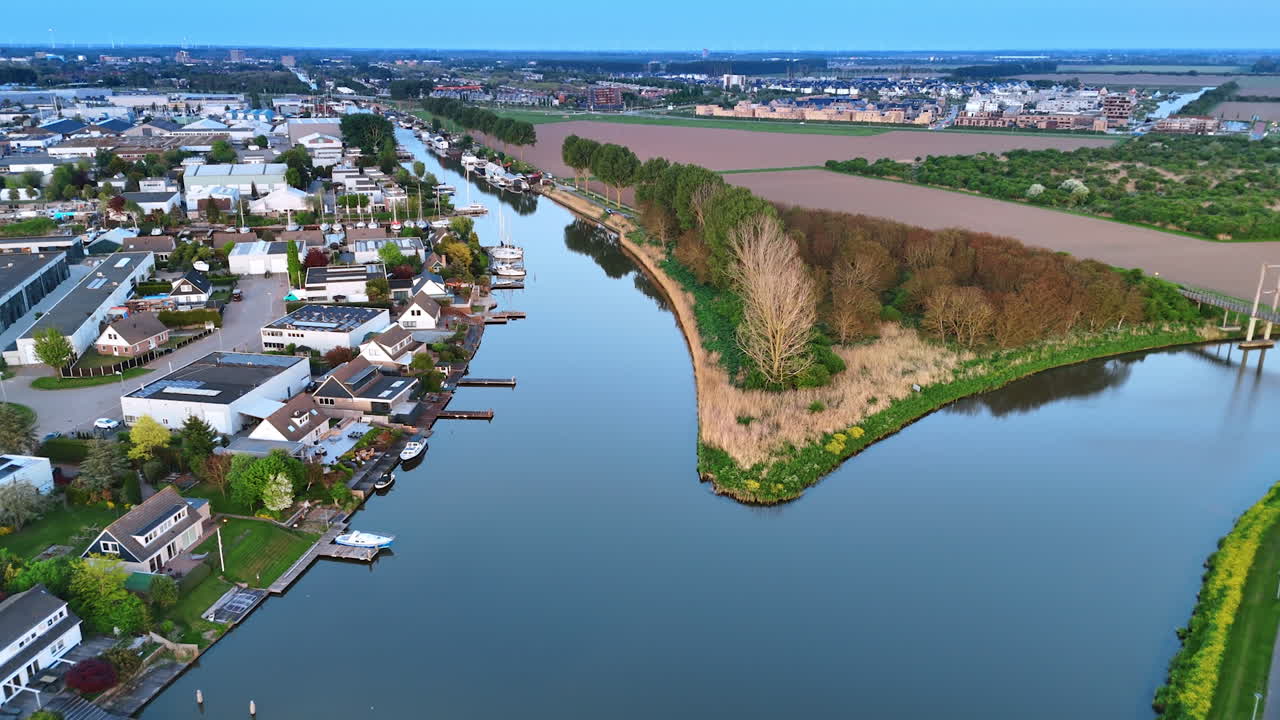 Flight over the mirror surface of the canal with little berths. Picturesque village on water in the countryside of the Netherlands.