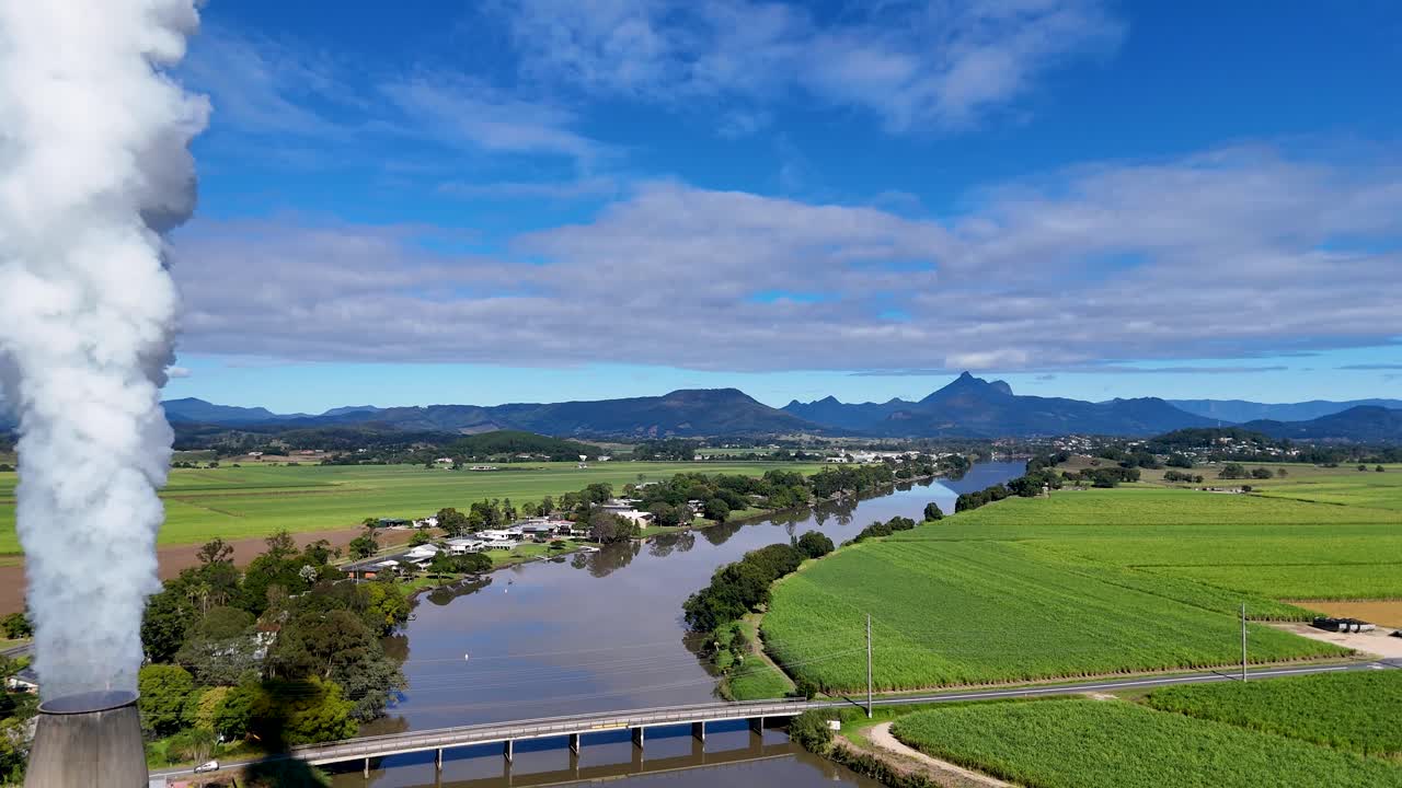 Drone footage captures a sugarcane field, factory, and river under clear skies, highlighting industrial and natural landscapes
