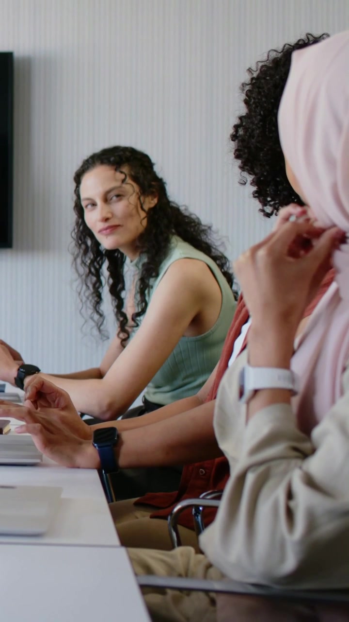 Video verticale: Inizio riunione, donna con hijab che si sistema il velo mentre il team scrive al computer in una stanza con portatili