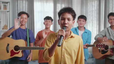 group of young asian friends with musical instruments waving hand and speaking at home