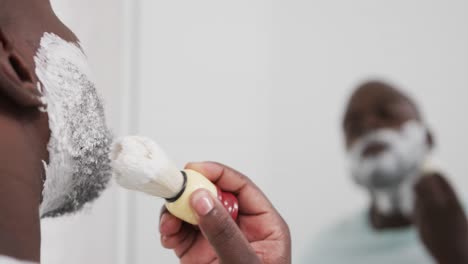 African-american-man-applying-shaving-cream-on-face-in-bathroom,-in-slow-motion