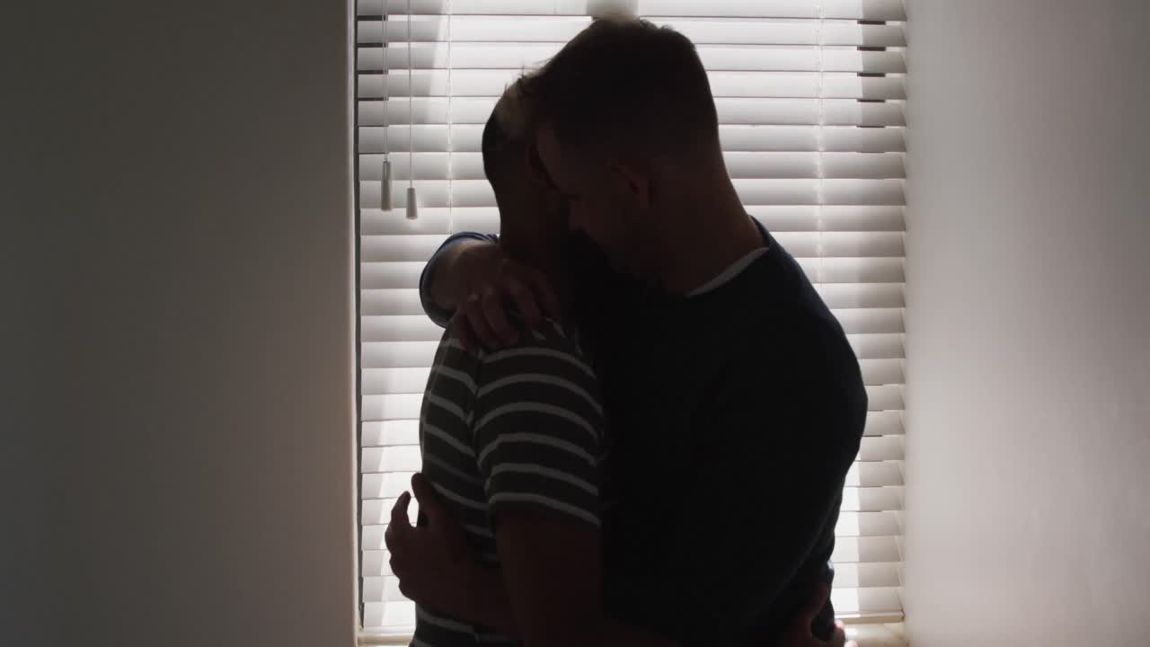 pareja de hombres homosexuales multiétnicos abrazándose por la ventana