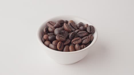 close-up of hand holding white cup with roasted coffee beans