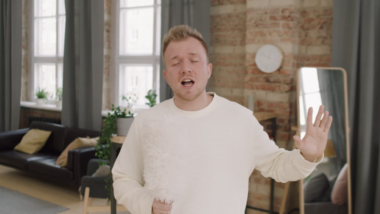 Young Man Singing into Dust Brush at Home